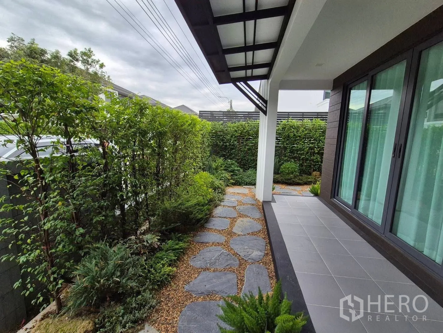 บ้าน ขายในBang Kruai, Nonthaburi - สวนข้างบ้านจัดแต่งด้วยทางเดินแผ่นหิน ไม้พุ่ม และชานระเบียงหลังคา