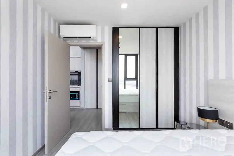 Condominium for rent in Phra Khanong, Bangkok - Bedroom wardrobe with mirrored sliding doors and striped feature wall.