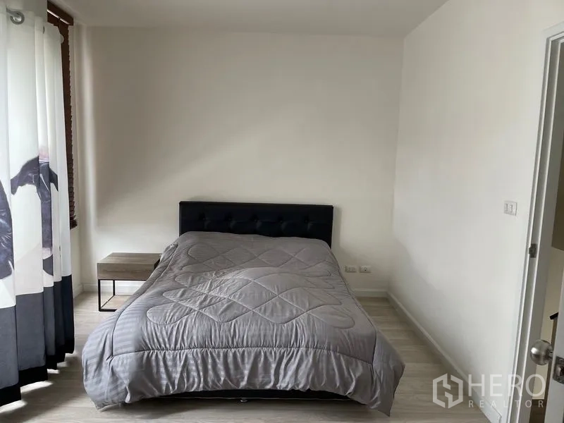 Townhouse for rent in Bang Kapi, Bangkok - Cozy bedroom with dark upholstered bed, bedside table and curtains.