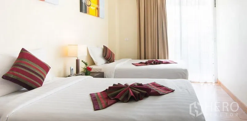 คอนโด ให้เช่าในKhlong Toei, Bangkok - ห้องนอนเตียงคู่ ปูผ้าขาวสะอาด หมอนตกแต่ง และโคมไฟหัวเตียง รับแสงธรรมชาติผ่านผ้าม่านสูง