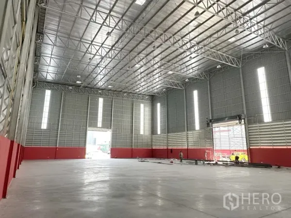 Warehouse for rent in Khlong Luang, Pathum Thani - Spacious warehouse interior showing high steel truss roof, polished concrete floor, skylight panels and a large roller door.