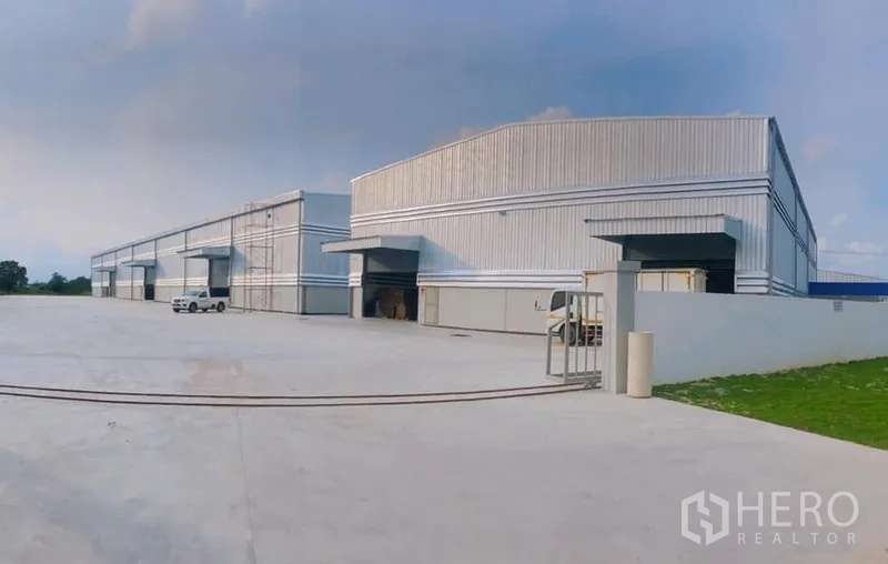 Warehouse for rent in Ban Bueng, Chon Buri - Exterior of large steel-clad warehouses featuring loading bays and an ample driveway.