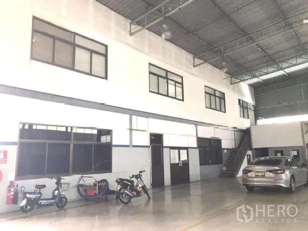 工厂 出租在Bang Bua Thong, Nonthaburi - 明亮厂房，设夹层办公室、混凝土地面与停放车辆。