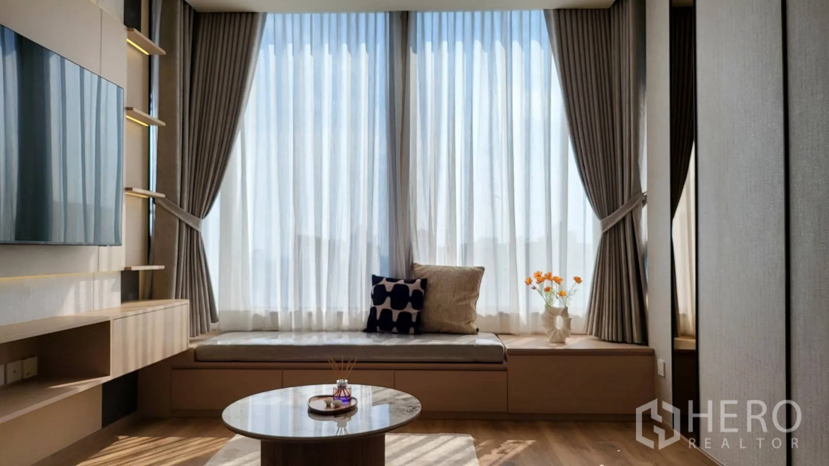 公寓 for sale in Watthana, Bangkok - 窗边座位与通高窗帘引入采光，旁有圆形茶几与电视墙。