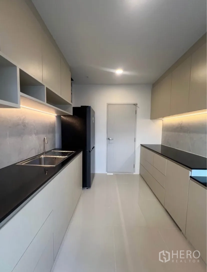 Detached House for rent in Bang Phli, Samut Prakan - Modern galley kitchen with black stone countertops, ample cabinetry, under-cabinet lighting and a refrigerator.