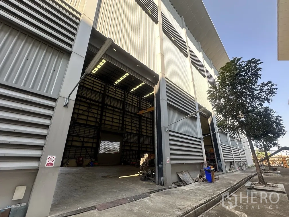 Factory for rent in Lam Luk Ka, Pathum Thani - Exterior of high-bay factory with wide roller shutter door open.