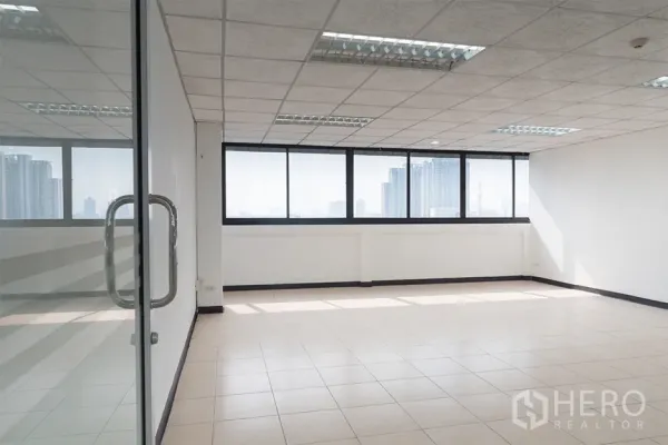 办公空间 出租在Din Daeng, Bangkok - 明亮的空置办公室，瓷砖地面、格栅天花与灯具，宽幅窗户可望曼谷天际线，从玻璃门内拍摄。