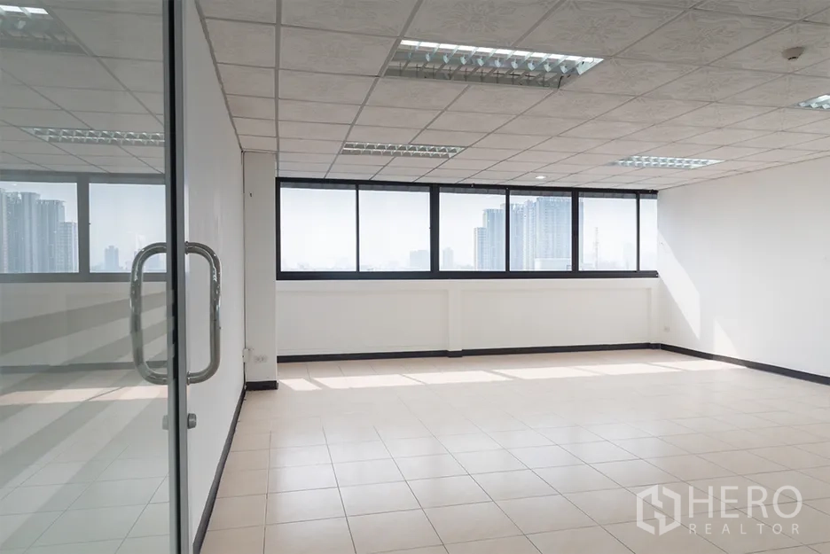 办公空间 出租在Din Daeng, Bangkok - 明亮的空置办公室，瓷砖地面、格栅天花与灯具，宽幅窗户可望曼谷天际线，从玻璃门内拍摄。