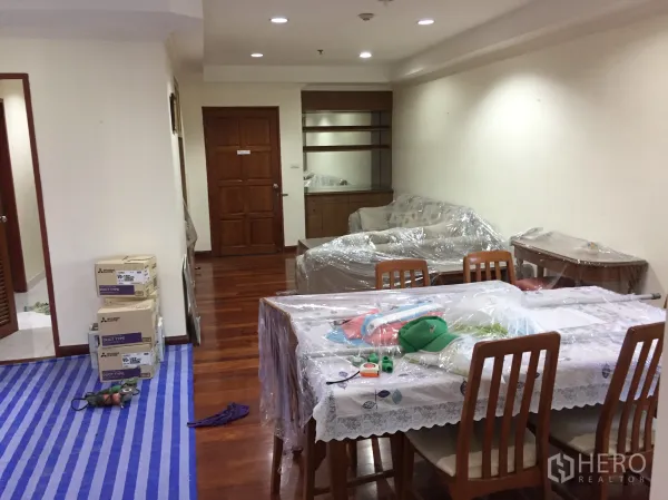 คอนโด ให้เช่าในWatthana, Bangkok - ห้องนั่งเล่นและรับประทานอาหารแบบเปิดโล่ง พื้นไม้จริง ไฟฝังฝ้า ชั้นวางบิวท์อิน และเฟอร์นิเจอร์คลุมพลาสติกเตรียมย้ายเข้า