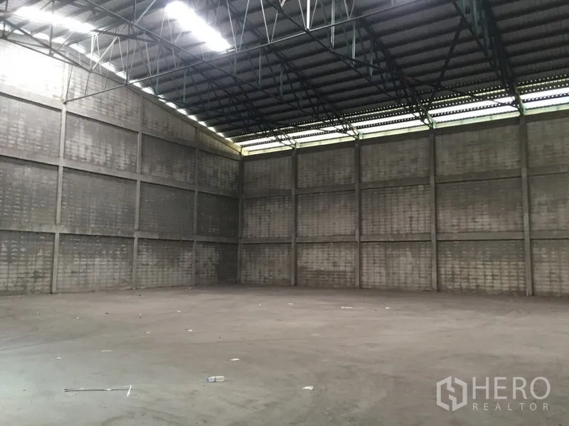 Warehouse for rent in Mueang Pathum Thani, Pathum Thani - Angle view of a clear-span warehouse interior with steel beams and smooth concrete flooring.