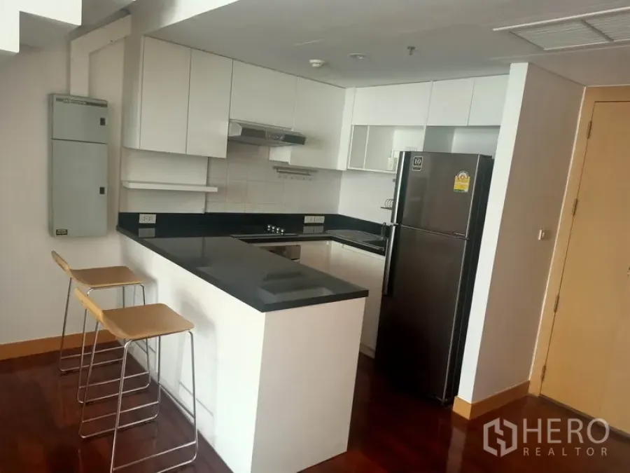 Condominium for rent in Watthana, Bangkok - Modern U-shaped kitchen with black granite counters, white cabinets, and a breakfast bar with two stools.