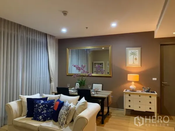 คอนโด ให้เช่าในWatthana, Bangkok - พื้นที่นั่งเล่นและรับประทานอาหารโทนอบอุ่น โซฟาสีครีม โต๊ะทานข้าว กระจกบานใหญ่ และแสงไฟนุ่มนวล