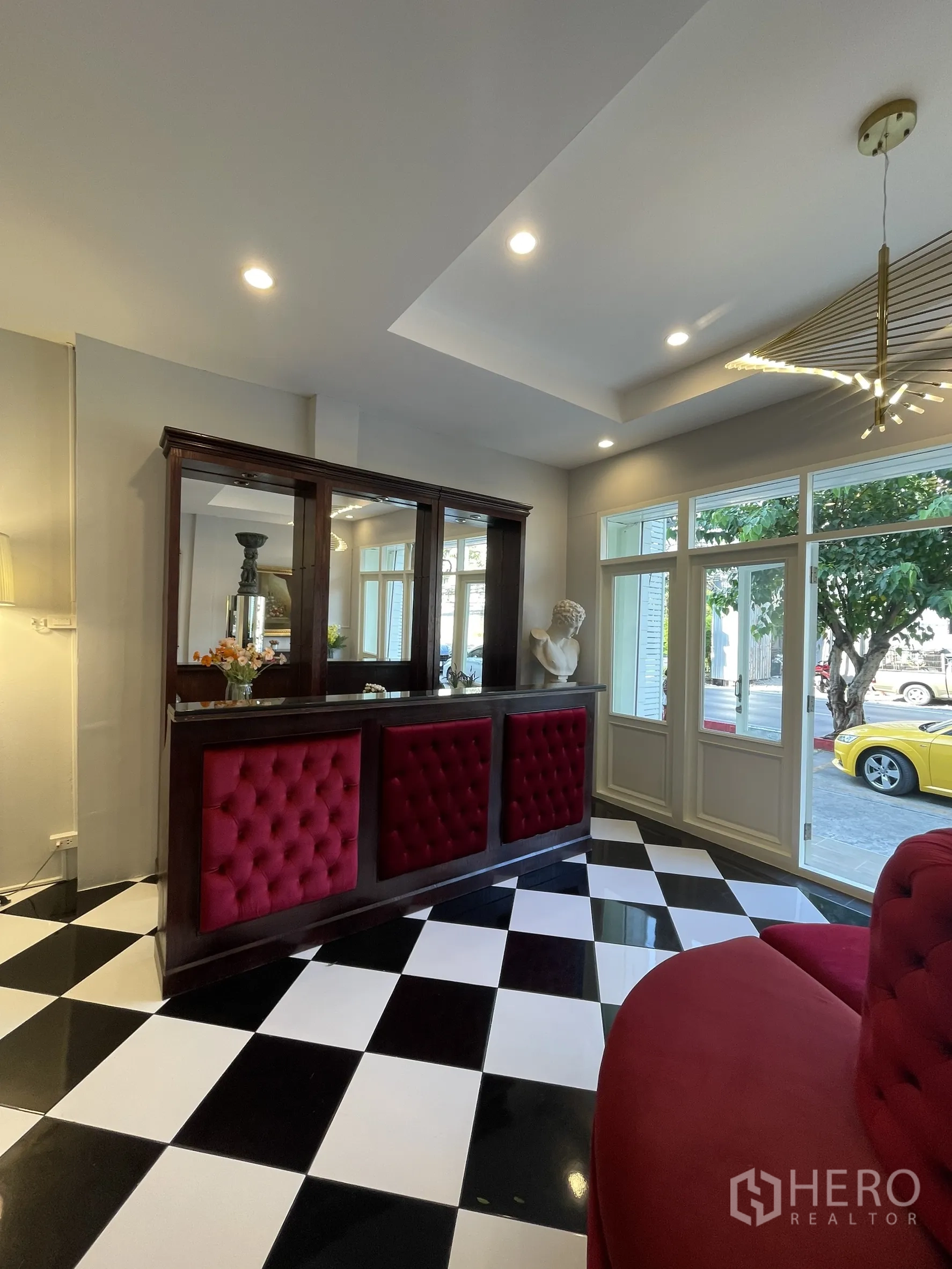 Shophouse for rent in Bang Kapi, Bangkok - Reception counter with tufted red panels beside large windows and black‑and‑white tile flooring.