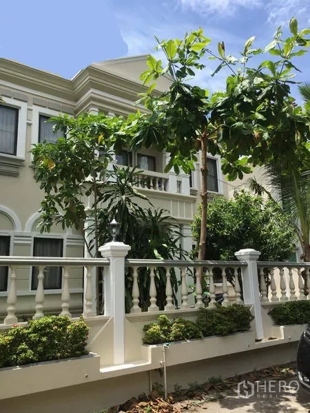 Detached House for rent in Khlong Toei, Bangkok - Neoclassical two-storey detached house facade with balcony, white balustrade and tropical trees.