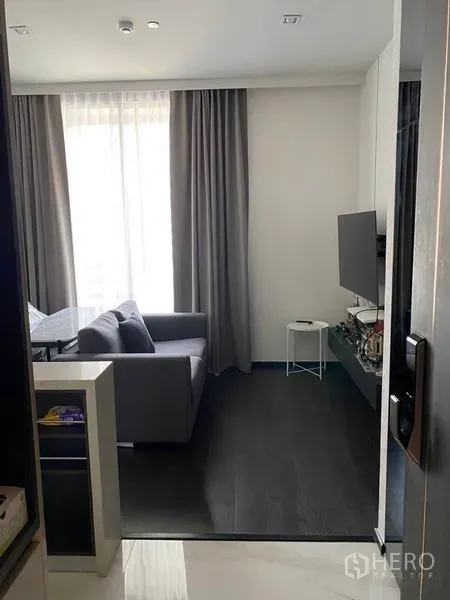 Condominium for rent in Watthana, Bangkok - Entrance view to a compact lounge with grey sofa, TV console and blackout curtains.