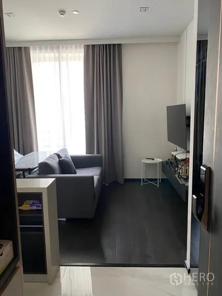 Condominium for rent in Watthana, Bangkok - Entrance view to a compact lounge with grey sofa, TV console and blackout curtains.