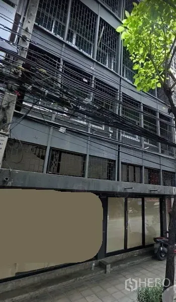 店屋 出租在Phra Khanong, Bangkok - 帕卡农多层商铺外立面，金属护栏与大面积玻璃门面，路旁树木与电缆，临近Bang Chak BTS。