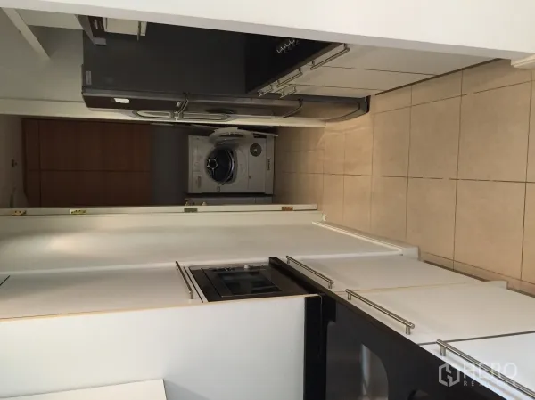 Condominium for rent or sale in Pathum Wan, Bangkok - Galley kitchen with white cabinetry, black countertops, built-in oven, large fridge and a washer–dryer.