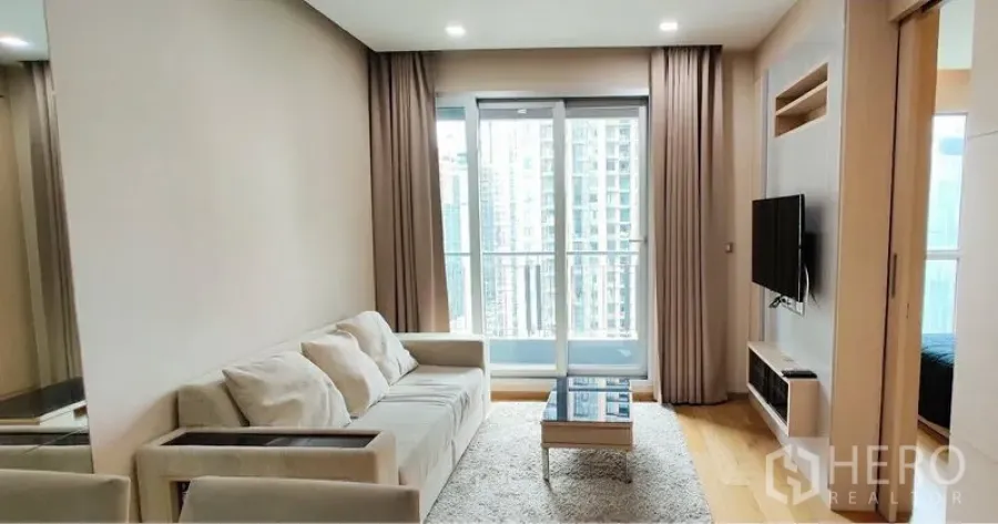 Condominium for rent in Ratchathewi, Bangkok - Bright living room with sofa, wall-mounted TV and balcony overlooking the Bangkok skyline.