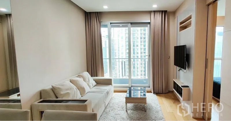 Condominium for rent in Ratchathewi, Bangkok - Bright living room with sofa, wall-mounted TV and balcony overlooking the Bangkok skyline.