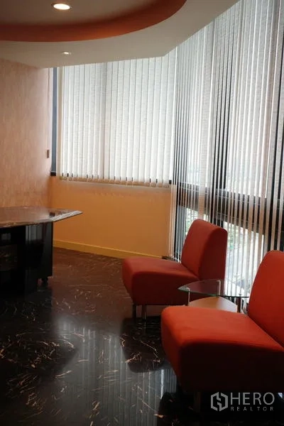 Office Space for rent in Bang Na, Bangkok - Lounge corner with two red chairs beside large windows with vertical blinds.