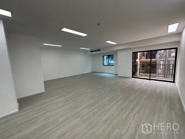 Office Space for rent - Open-plan office interior with wood-look flooring, recessed LED lighting, a window and sliding glass door to a small balcony.