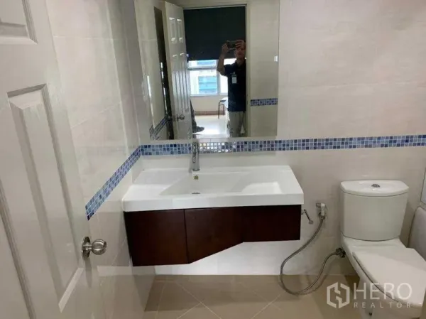 公寓 出租在Bang Rak, Bangkok - 浴室配大镜面、白色洗手台、蓝色马赛克腰线与坐便器。