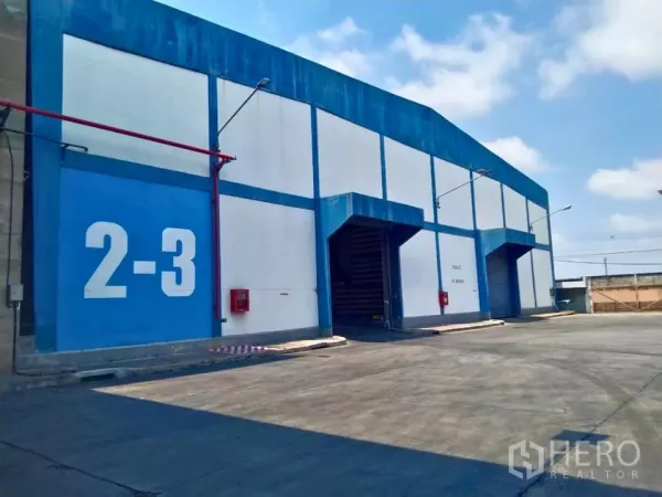 工厂 出租在Samut Prakan - 蓝白色工厂外观，卷帘门装卸月台与宽阔卡车通道。