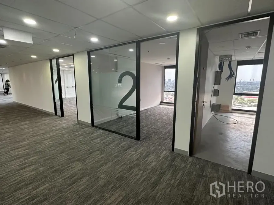 Office Space for rent in Khlong Toei, Bangkok - Corridor with numbered glass offices and a server room under installation, city view beyond.