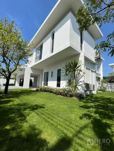 Detached House for rent in Samut Prakan - Corner exterior view of the white detached house and green lawn.