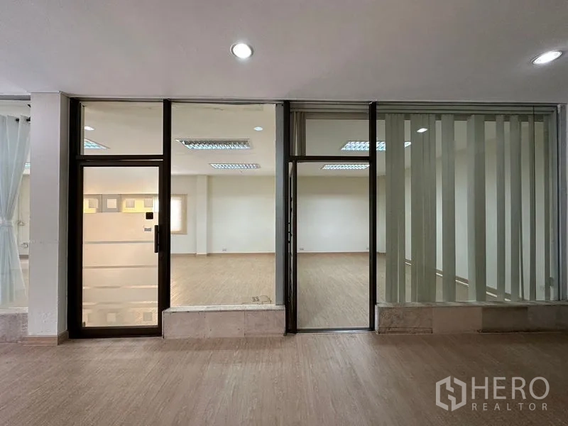 Warehouse for rent in Suan Luang, Bangkok - Glass storefront with framed door and vertical blinds opening to a bright office area.