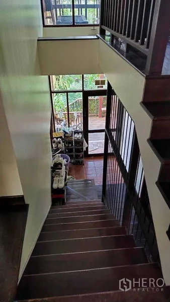 Detached House for sale in Suan Luang, Bangkok - Wooden staircase with railing leading to a glass door entry, shoe racks and garden view.