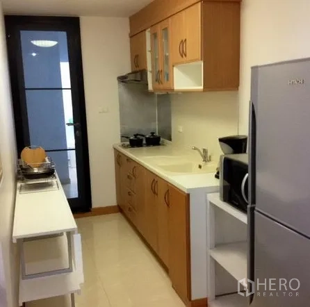 Condominium for rent in Watthana, Bangkok - Separate galley kitchen with wood cabinets, sink, microwave, and a full-size refrigerator.