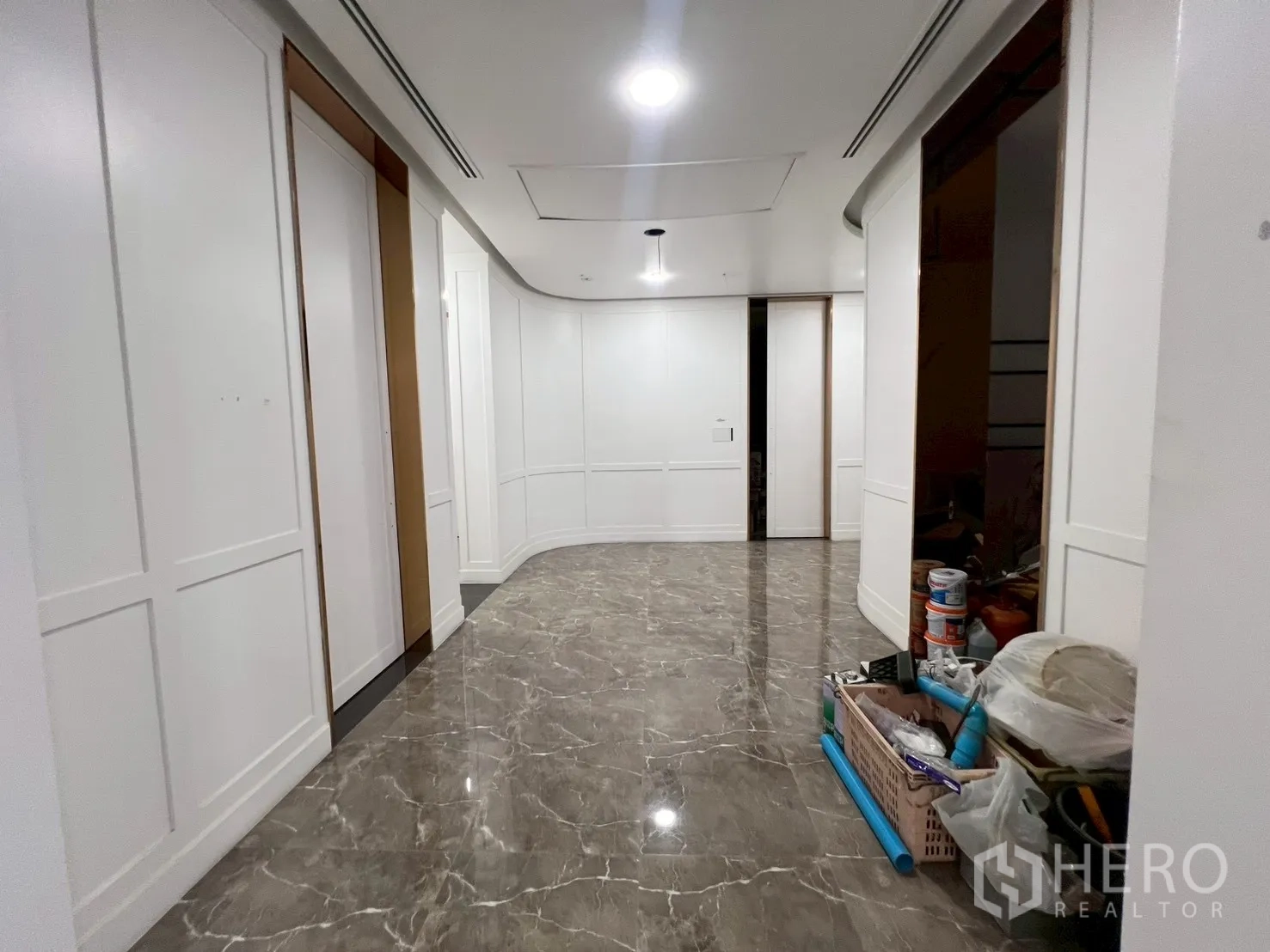 零售空间 出租在Watthana, Bangkok - 弧形走廊，白色墙板与大理石地砖，角落有工具与油漆