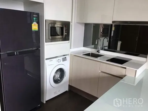 Condominium for rent in Ratchathewi, Bangkok - Modern kitchenette with refrigerator, microwave, washer, sink and dual cooktop.