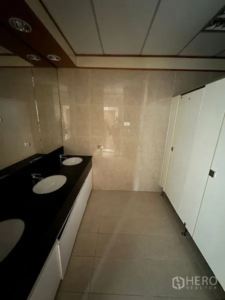 办公空间 出租在Pathum Wan, Bangkok - 卫生间配黑色石材台面、下嵌式洗手盆、镜面与白色隔间。