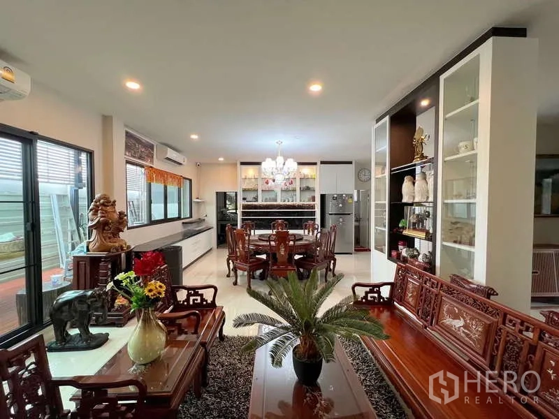 Detached House for sale in Prawet, Bangkok - Living area perspective showing carved wood seating, display shelves, and bright windows.