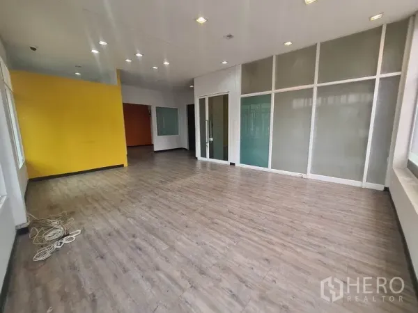 零售空间 出租在Watthana, Bangkok - 宽敞展厅，黄色特色墙、嵌灯与玻璃隔间。