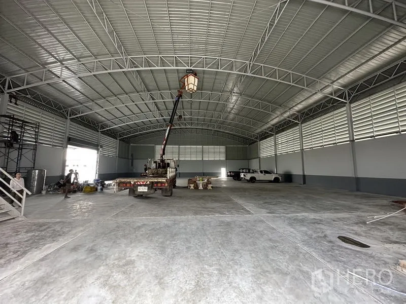 Factory for rent in Pathum Thani - Wide concrete factory space with central lighting beneath curved steel trusses.