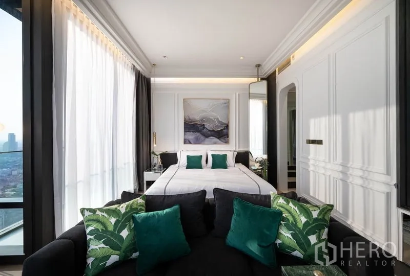 公寓 出租在Bang Rak, Bangkok - 从沙发望向卧室，白色墙板、高窗与绿色抱枕点缀。