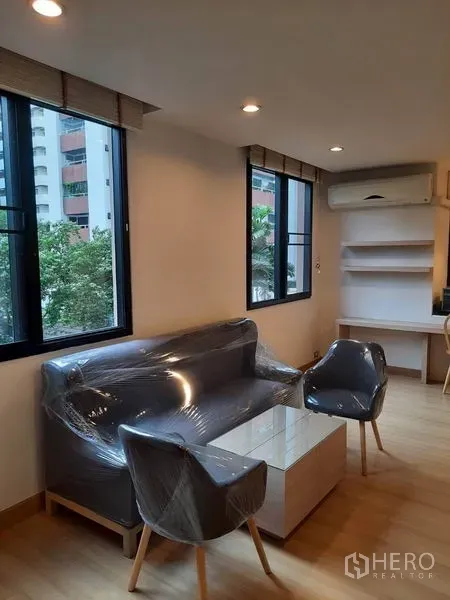 คอนโด ให้เช่าในWatthana, Bangkok - มุมรับแขกสว่างด้วยหน้าต่างบานใหญ่ โซฟา เก้าอี้ ชั้นวางบิลท์อิน และเครื่องปรับอากาศ มองเห็นต้นไม้
