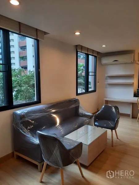 คอนโด ให้เช่าในWatthana, Bangkok - มุมรับแขกสว่างด้วยหน้าต่างบานใหญ่ โซฟา เก้าอี้ ชั้นวางบิลท์อิน และเครื่องปรับอากาศ มองเห็นต้นไม้