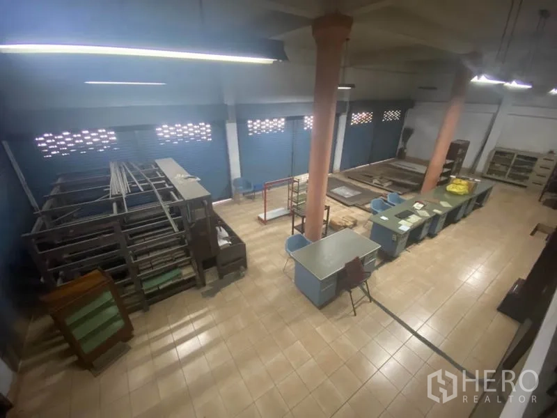 Warehouse for rent in Suan Luang, Bangkok - Ground-floor storage area with tiled floor, work tables and metal roller shutters.