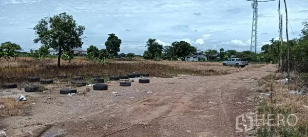 Land for sale in Bang Bo, Samut Prakan - Dirt access road across an open field with a pickup truck, scattered tires and a distant communication mast.