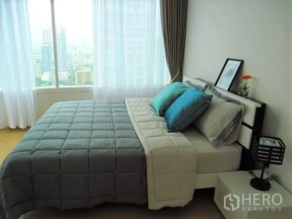 Condominium for rent or sale in Watthana, Bangkok - Corner master bedroom with double bed, teal pillows and wide city skyline views through large windows.