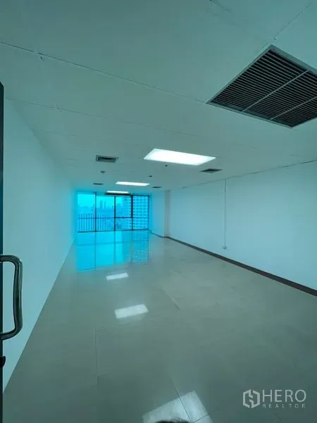 办公空间 出租在Huai Khwang, Bangkok - 长形开放式办公室，亮面地砖、吊顶灯与空调出风口，尽头为通阳台的推拉玻璃门，可见城市景观，近MRT Sutthisan。