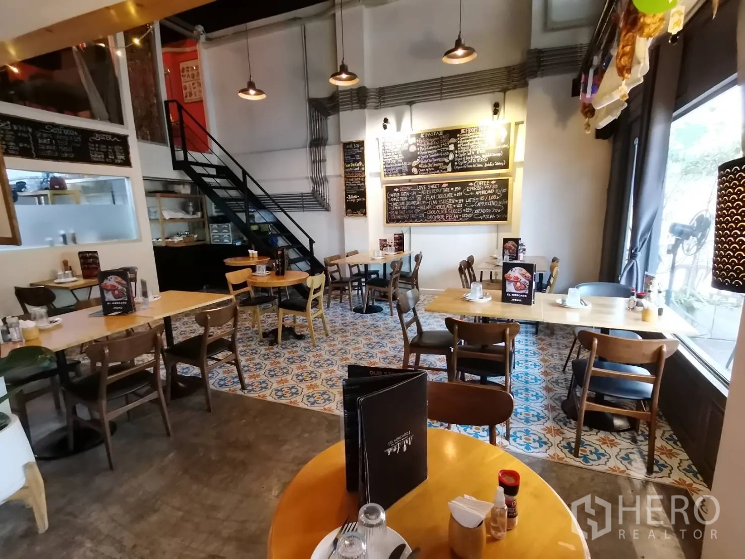 零售空间 出租在Watthana, Bangkok - 用餐区，花纹地砖、菜单黑板与金属楼梯。