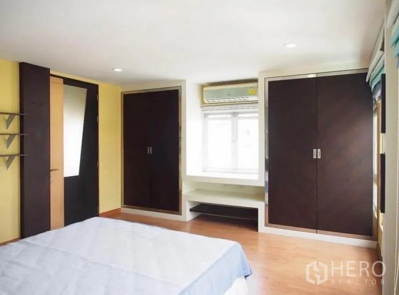 Townhouse for rent in Wang Thonglang, Bangkok - Bedroom with twin built-in wardrobes, bay window seat, air conditioner and wooden floors.