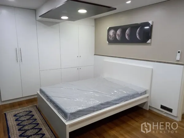 公寓 出租在Khlong Toei, Bangkok - 主卧配白色床架与大容量嵌入式衣柜，墙上月相装饰画。