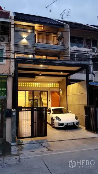 Townhouse for rent in Khlong Toei, Bangkok - Three-storey townhouse exterior at dusk with gated carport and a parked white car.